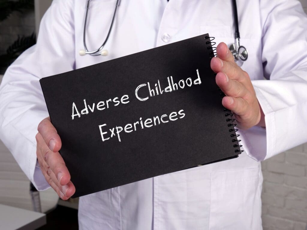 A physician holding an adverse childhood experiences sign. The office of Ginny Estupinian PhD treats adverse childhood trauma