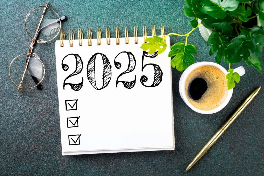 photo of a notebook and, cup of coffee, pen, and glasses depicting preparing to write goals for 2025