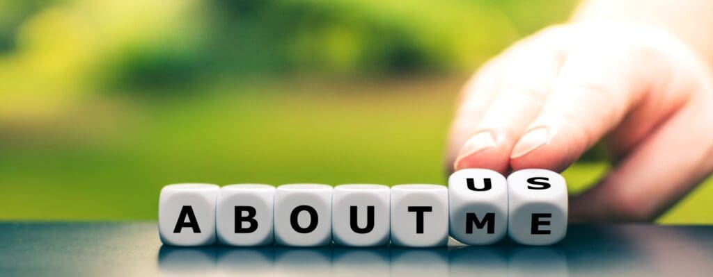 Hand flipping a dice to change the phrase 'About Me' to 'About Us', symbolizing the shift from self-focus to relational awareness—concepts central to understanding narcissism and its impact on relationships
